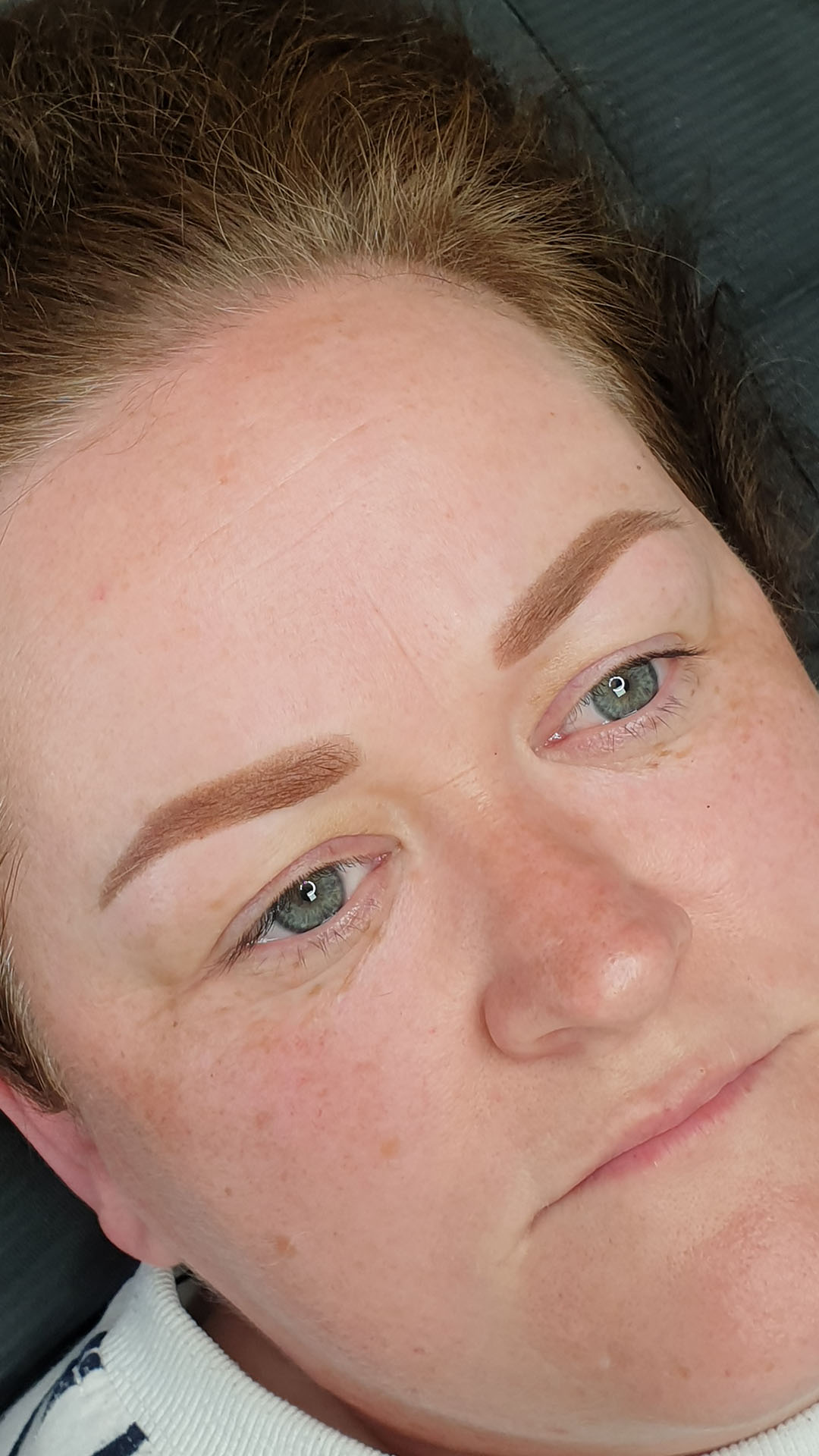 A woman with long brown hair and gold hoop earrings, featured in a semi-permanent makeup after