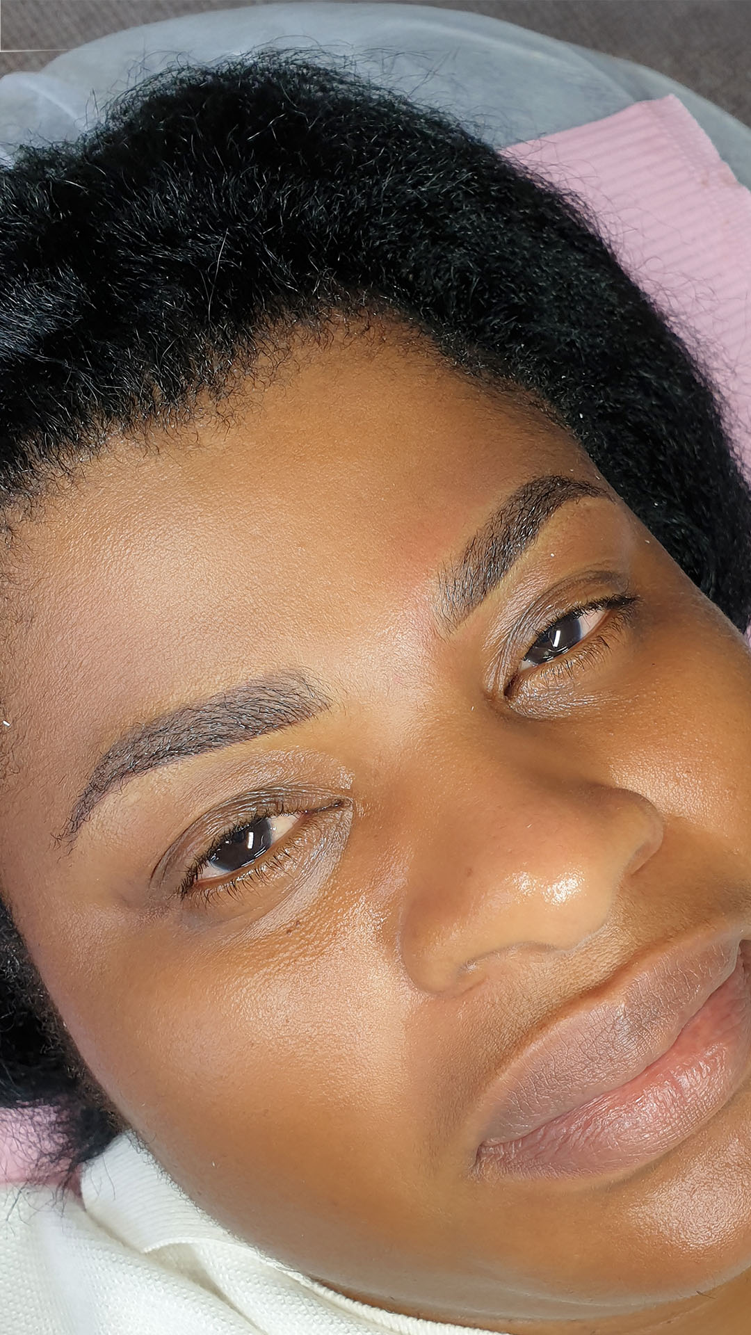 A woman relaxing in a chair with her eyes closed, showcasing a serene moment after her semi-permanent makeup session