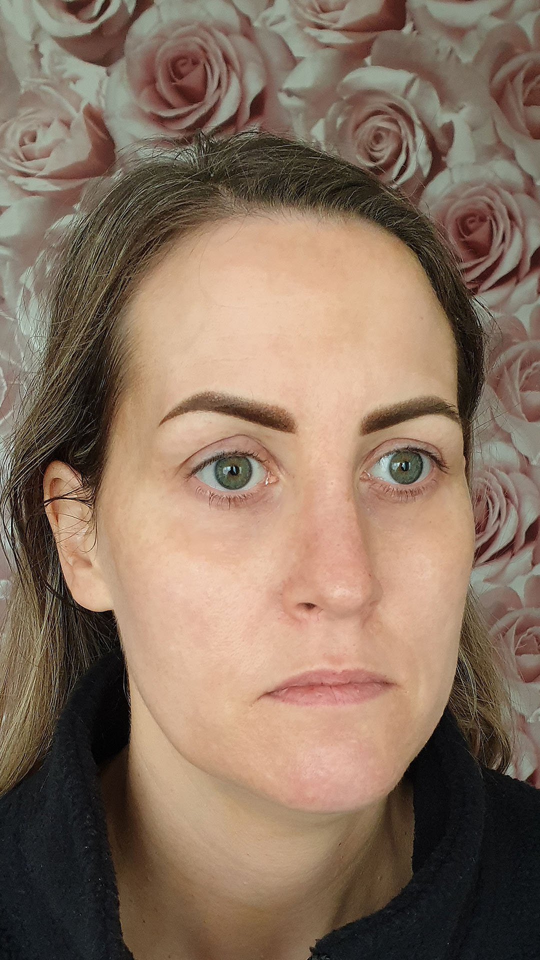 Woman with neatly styled eyebrows lying on a pink and gray surface, wearing a white top-after